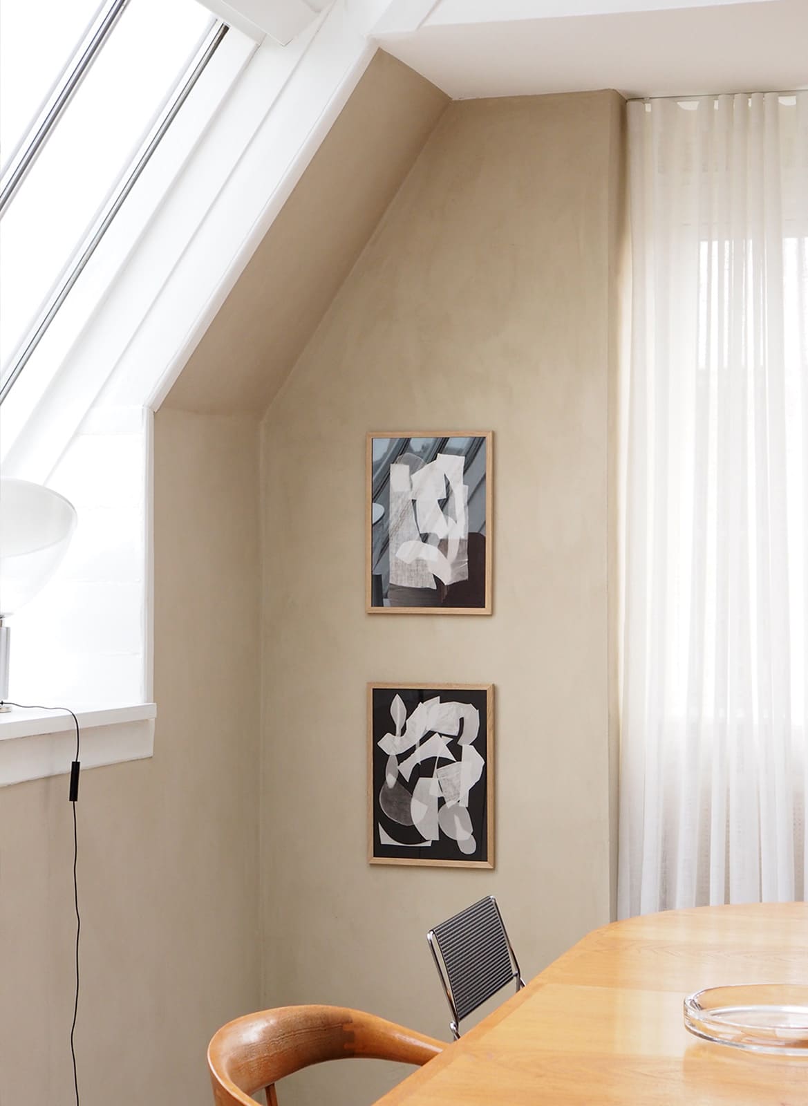 Framed black and white posters hanging above dining table by Atelier Cph