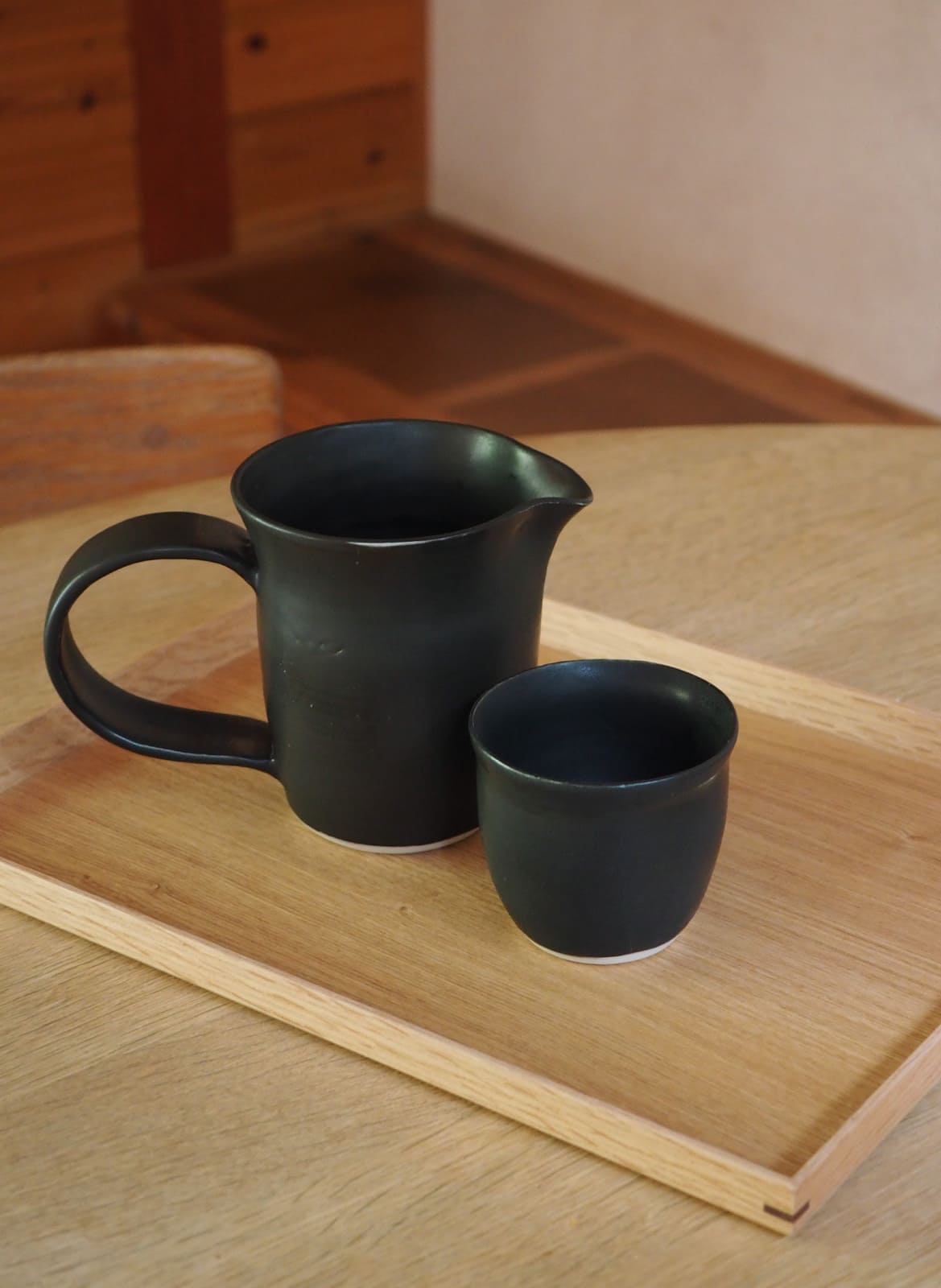 handmade black ceramic jug and cup standing on a wooden table